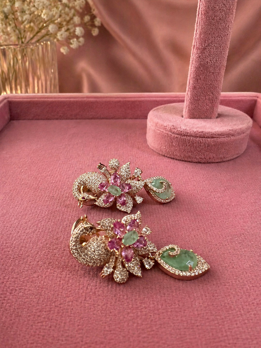 Swan motif emerald and pink stone statement earrings displayed on stand for wedding and festive wear